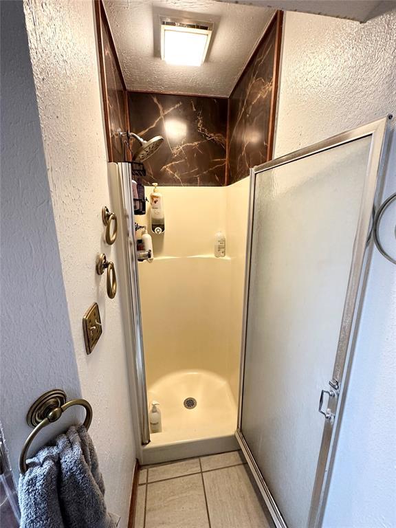 bathroom featuring an enclosed shower, tile patterned flooring, and a textured ceiling