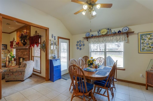 tiled dining space featuring lofted ceiling, a brick fireplace, and ceiling fan