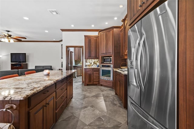 kitchen with crown molding, stainless steel appliances, tasteful backsplash, light stone counters, and a kitchen island