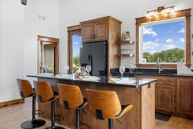 kitchen featuring sink, a kitchen bar, a center island, light hardwood / wood-style floors, and black refrigerator with ice dispenser