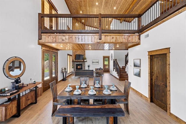 dining area featuring a high ceiling, wood ceiling, a fireplace, and light hardwood / wood-style flooring