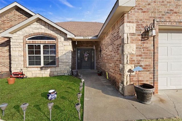 doorway to property featuring a garage, a shingled roof, stone siding, a yard, and brick siding