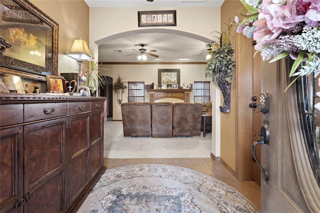 entryway featuring light tile patterned floors, arched walkways, light colored carpet, ceiling fan, and ornamental molding