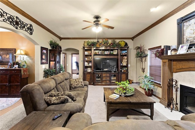 carpeted living area with a fireplace with flush hearth, arched walkways, ornamental molding, and a ceiling fan