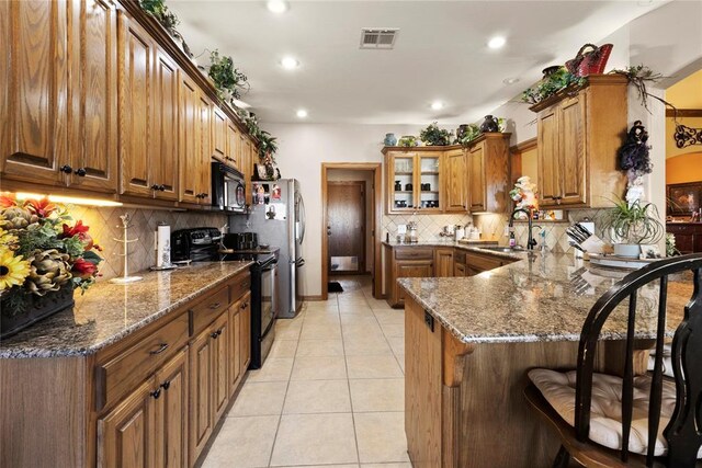 kitchen featuring a peninsula, a sink, visible vents, black appliances, and a kitchen bar