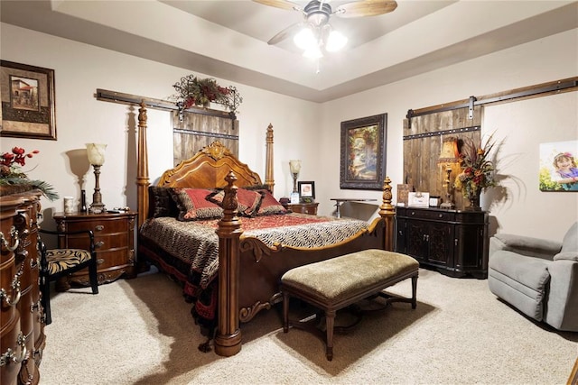 bedroom featuring a tray ceiling, carpet flooring, ceiling fan, and a barn door