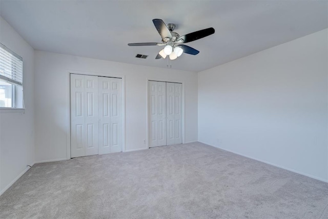 unfurnished bedroom with ceiling fan, light carpet, and two closets