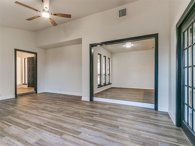 spare room with a ceiling fan, light wood-type flooring, visible vents, and baseboards