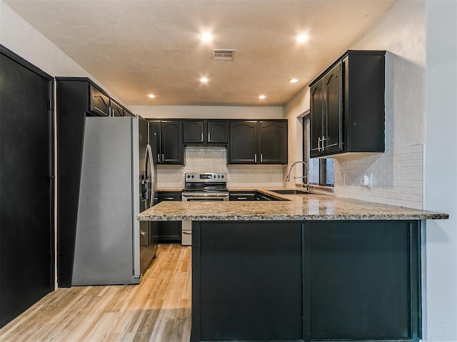 kitchen featuring light stone counters, stainless steel appliances, a peninsula, a sink, and light wood finished floors