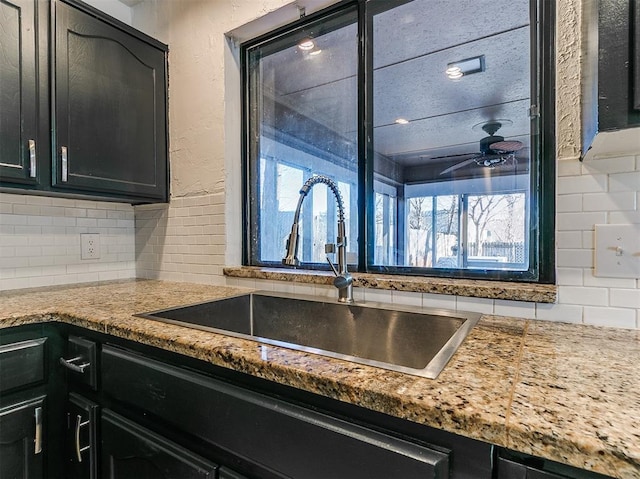 kitchen with dark cabinetry, a sink, backsplash, and ceiling fan