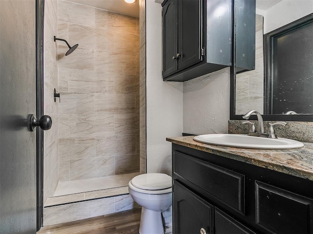 full bath with wood finished floors, tiled shower, vanity, and toilet