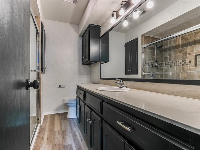 bathroom with a textured wall, toilet, a stall shower, vanity, and wood finished floors