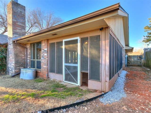 back of property with a sunroom, a chimney, fence, and brick siding