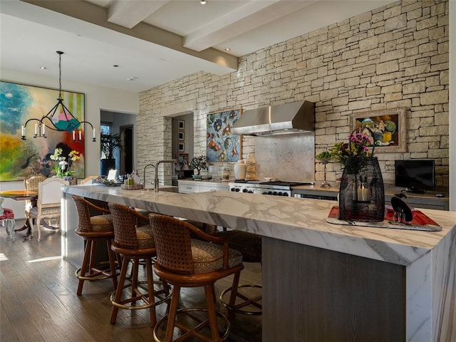 interior space with beamed ceiling, wall chimney exhaust hood, range, and a breakfast bar area