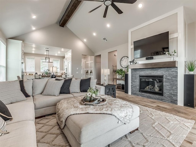 living room with high vaulted ceiling, a fireplace, beamed ceiling, ceiling fan, and light hardwood / wood-style floors