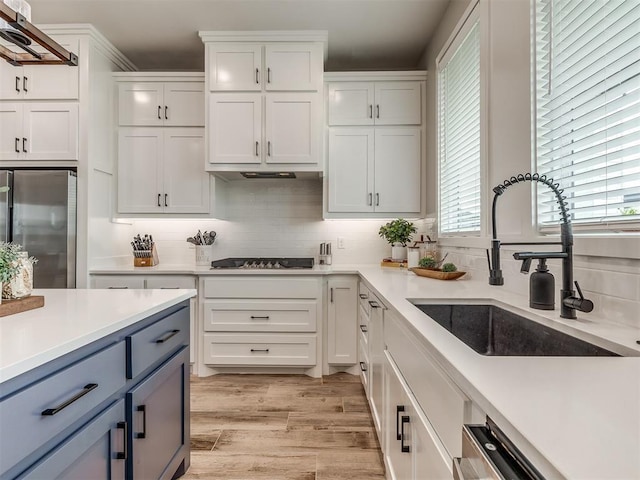 kitchen featuring stainless steel refrigerator, sink, white cabinets, decorative backsplash, and black gas stovetop