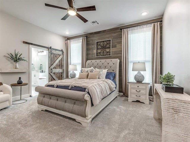 carpeted bedroom featuring ensuite bath, wooden walls, a barn door, and ceiling fan