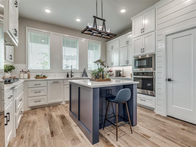 15417 Jasper Ln, Edmond, OK 73013 - kitchen with white cabinets, light wood-type flooring, a center island, a kitchen bar, and appliances with stainless steel finishes