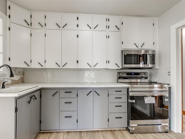 kitchen with appliances with stainless steel finishes, sink, decorative backsplash, and light wood-type flooring