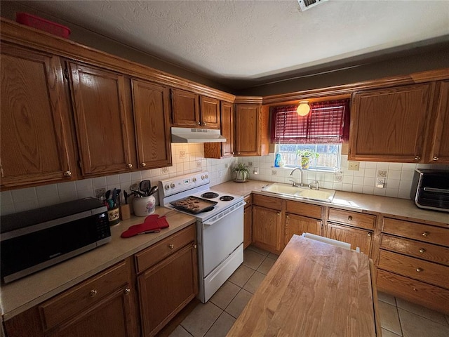 kitchen with white electric stove, light tile patterned floors, under cabinet range hood, a sink, and stainless steel microwave