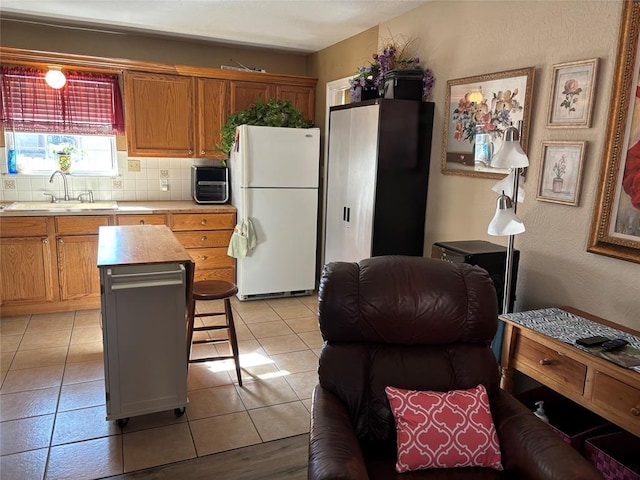 kitchen with light tile patterned floors, light countertops, backsplash, freestanding refrigerator, and a sink