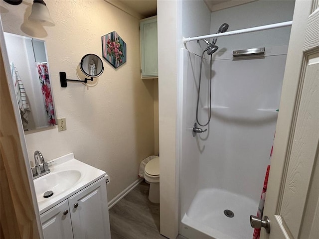 bathroom featuring a stall shower, baseboards, toilet, wood finished floors, and vanity