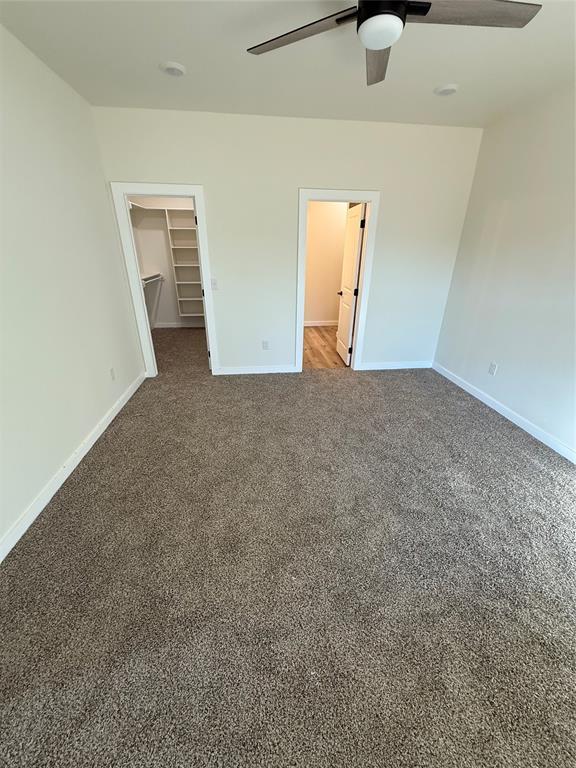 unfurnished bedroom featuring dark colored carpet, ceiling fan, a closet, and a walk in closet