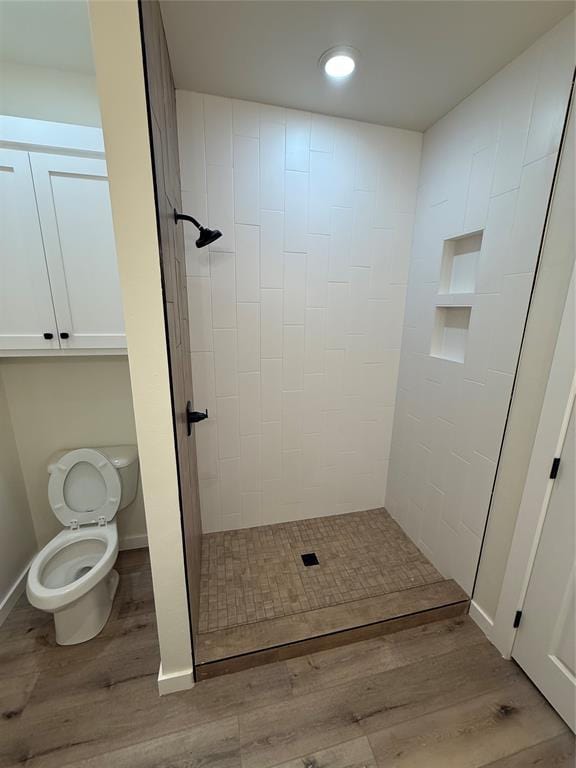 bathroom featuring a tile shower, wood-type flooring, and toilet