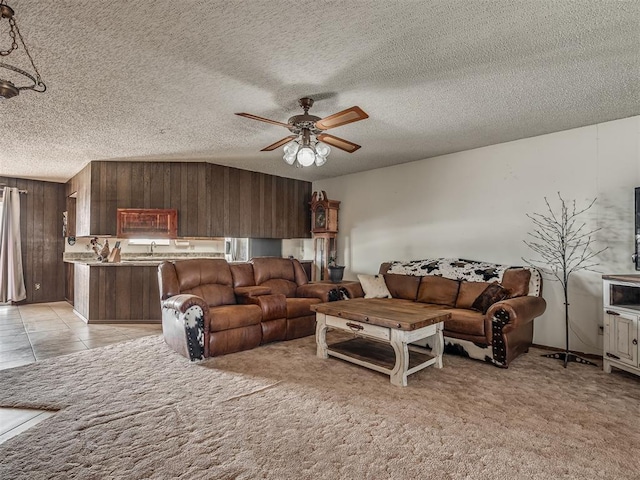 carpeted living room with ceiling fan, wooden walls, and a textured ceiling