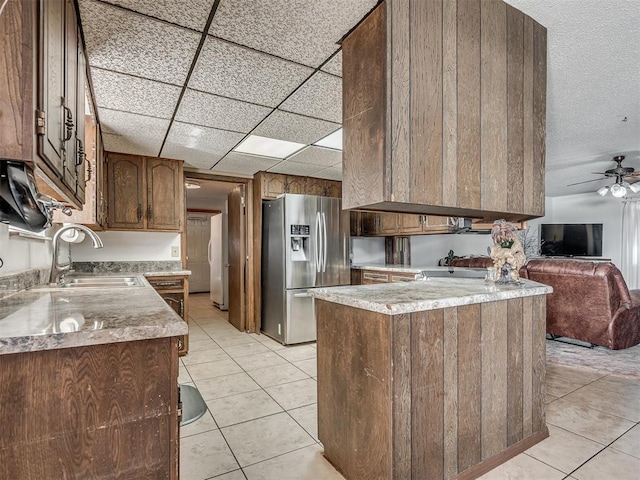 kitchen featuring sink, light tile patterned floors, kitchen peninsula, stainless steel refrigerator with ice dispenser, and a drop ceiling