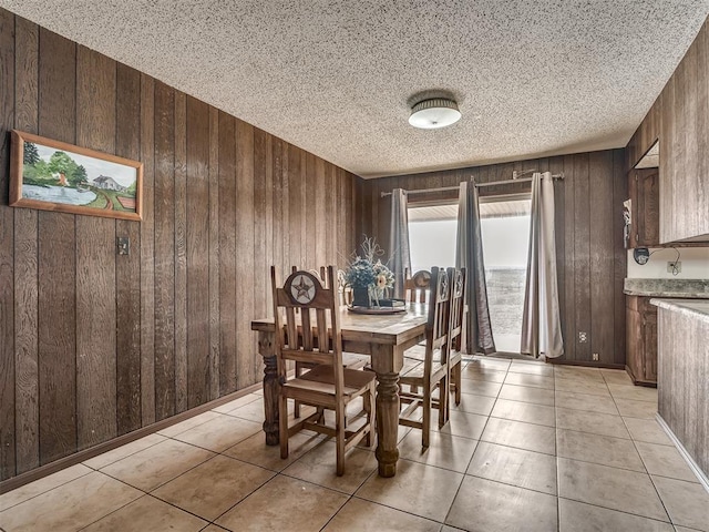 dining space featuring light tile patterned floors, wooden walls, and a textured ceiling