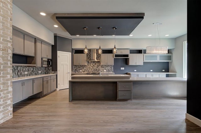 1548 NW 175th Ct, Edmond, OK 73012 - kitchen with stainless steel microwave, wall chimney exhaust hood, a center island with sink, decorative backsplash, and light wood-style floors
