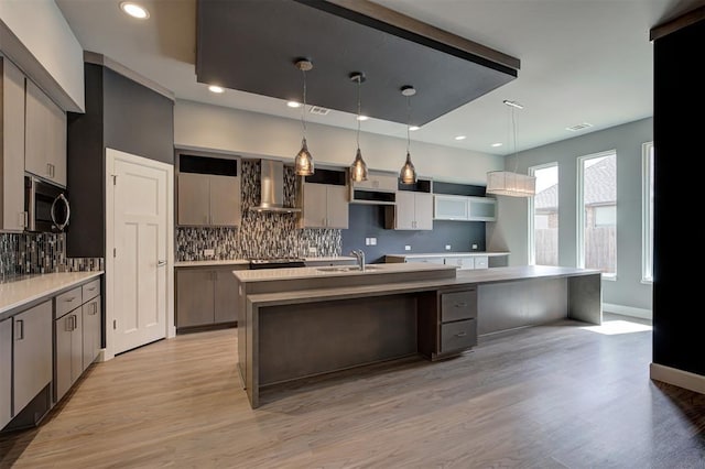 1548 NW 175th Ct, Edmond, OK 73012 - kitchen with stainless steel microwave, wall chimney exhaust hood, a center island with sink, tasteful backsplash, and light wood finished floors