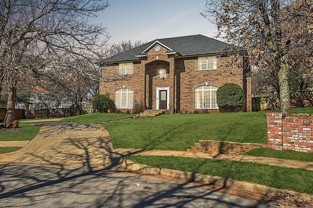 view of front of house with a front yard, brick siding, and a shingled roof