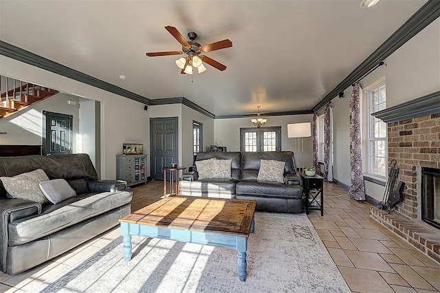 living area featuring ceiling fan with notable chandelier, crown molding, baseboards, a brick fireplace, and stairs