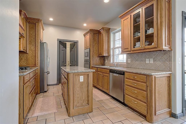 kitchen with a sink, glass insert cabinets, appliances with stainless steel finishes, tasteful backsplash, and a center island