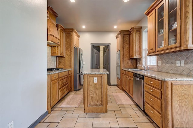 kitchen featuring recessed lighting, stainless steel appliances, brown cabinetry, glass insert cabinets, and light stone countertops