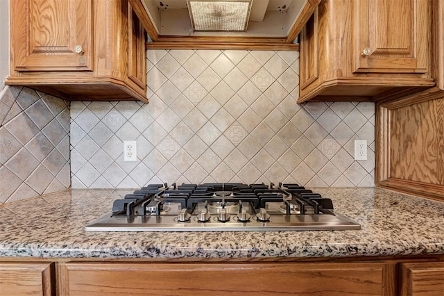 kitchen featuring backsplash, ventilation hood, light stone countertops, stainless steel gas stovetop, and brown cabinetry