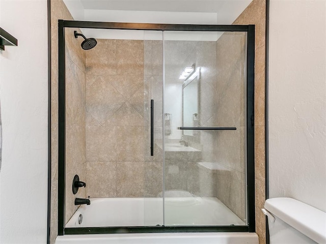 full bath with enclosed tub / shower combo, toilet, and a textured wall