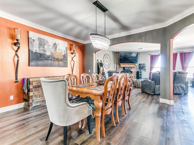 dining area with wood finished floors, arched walkways, a brick fireplace, and ornamental molding