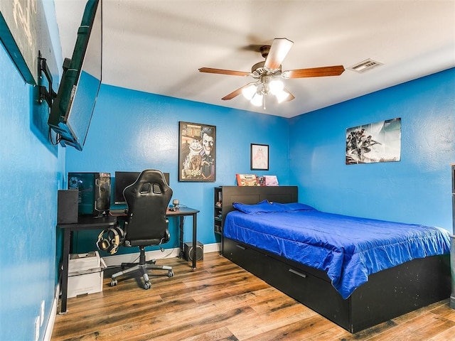 bedroom featuring a ceiling fan, wood finished floors, visible vents, and baseboards