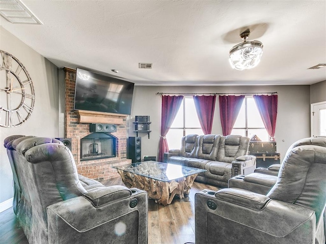 living area featuring a brick fireplace, wood finished floors, and visible vents