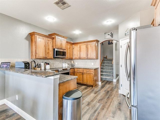 kitchen featuring light wood-type flooring, visible vents, backsplash, appliances with stainless steel finishes, and a peninsula