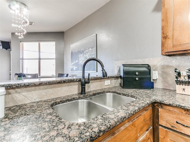 interior details featuring visible vents, dark stone counters, a sink, brown cabinets, and backsplash