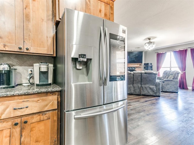 kitchen with wood finished floors, dark stone counters, stainless steel fridge with ice dispenser, tasteful backsplash, and open floor plan