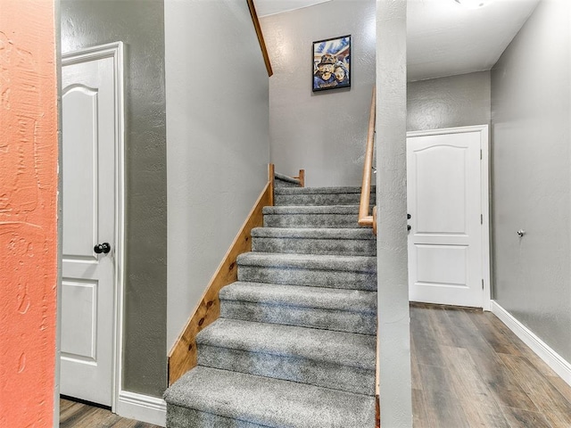 stairs featuring wood finished floors, baseboards, and a textured wall