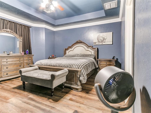 bedroom featuring a raised ceiling, wood finished floors, visible vents, and ceiling fan