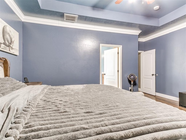 bedroom featuring visible vents, wood finished floors, a tray ceiling, and ornamental molding