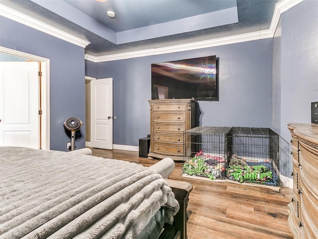 bedroom with crown molding, a tray ceiling, and wood finished floors