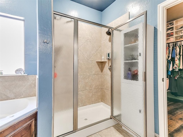 full bathroom with a walk in closet, a bath, a textured wall, and a stall shower